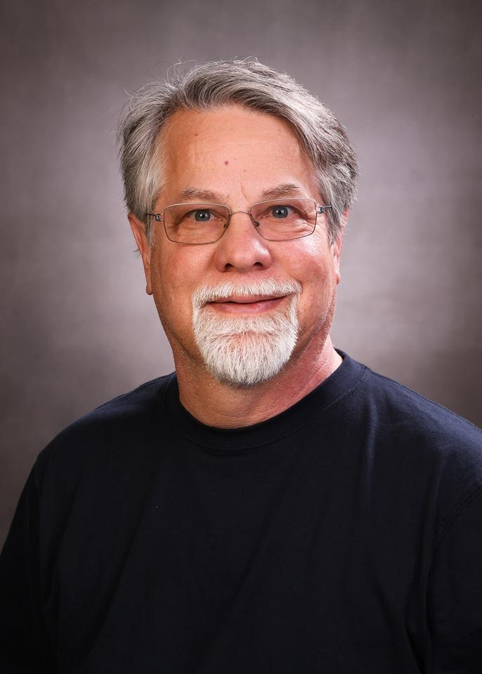 headshot of Evan K. Wallace, a man with short gray hair, a gray beard, and glasses.