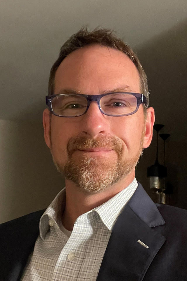 smiling man in black suit wearing glasses