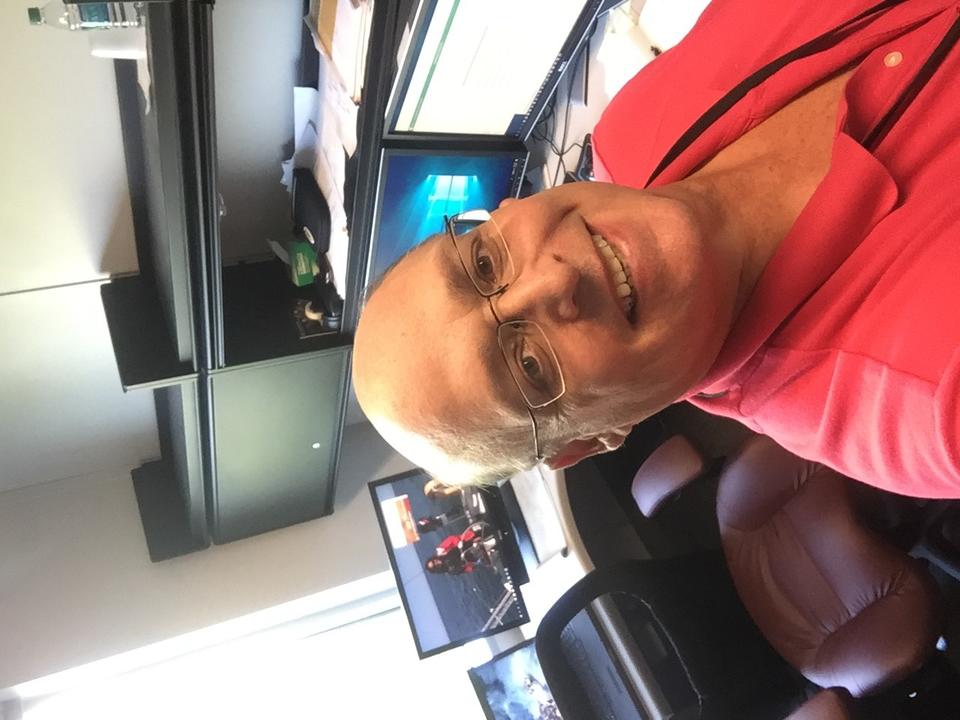 man sitting in an office wearing a read collared shirt and glasses 