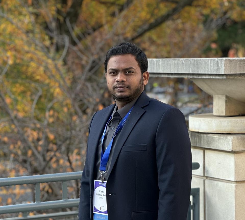 Man wearing a dark suit standing by trees in the fall season