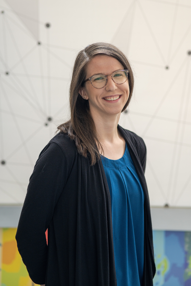 Picture of a smiling woman with brown hair wearing glasses and a blue shirt with a cardigan.