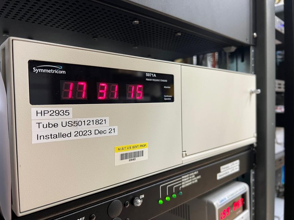 A tan rectangular box with a digital readout (17 31 15) sits on a server rack. 