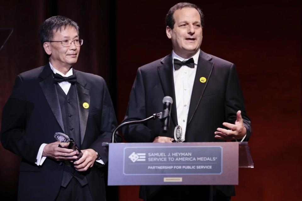 NIST researchers Long Phan and Marc Levitan stand at a podium after accepting their Service to America medals.