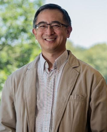 Man with glasses and dark hair wearing a tan shirt and tan jacket.