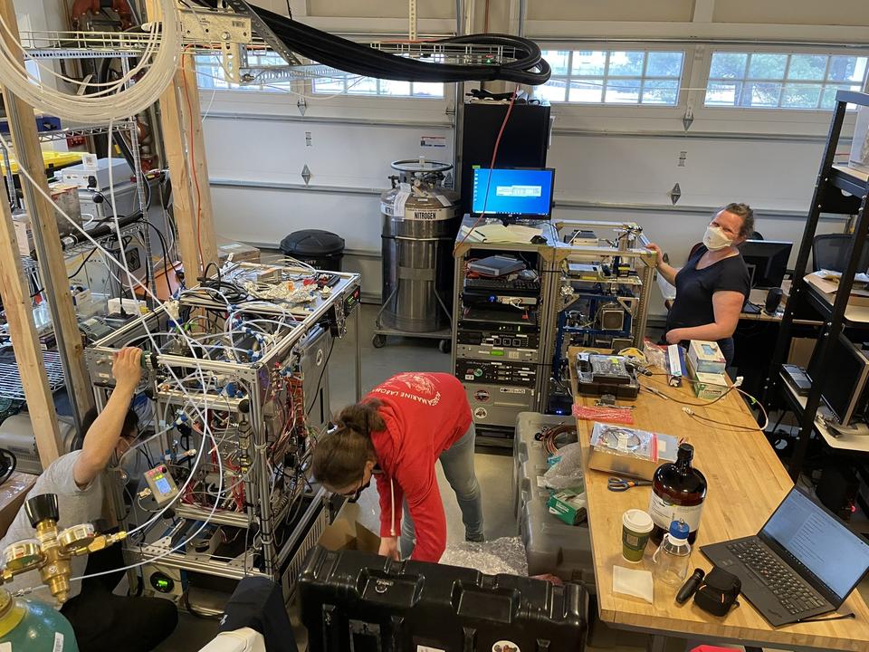 The inside of a two-car garage is filled with racks of equipment and wiring, with three researchers working to arrange the equipment. 