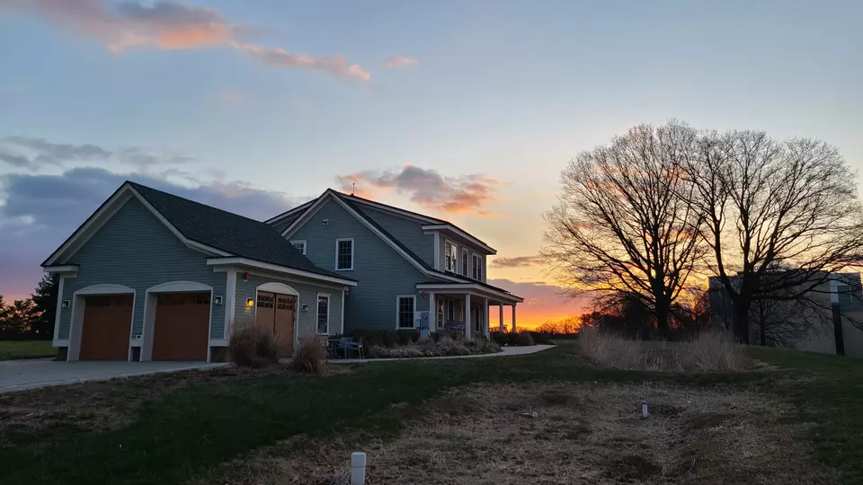 The net-zero house and nearby trees are silhouetted against the setting sun. 