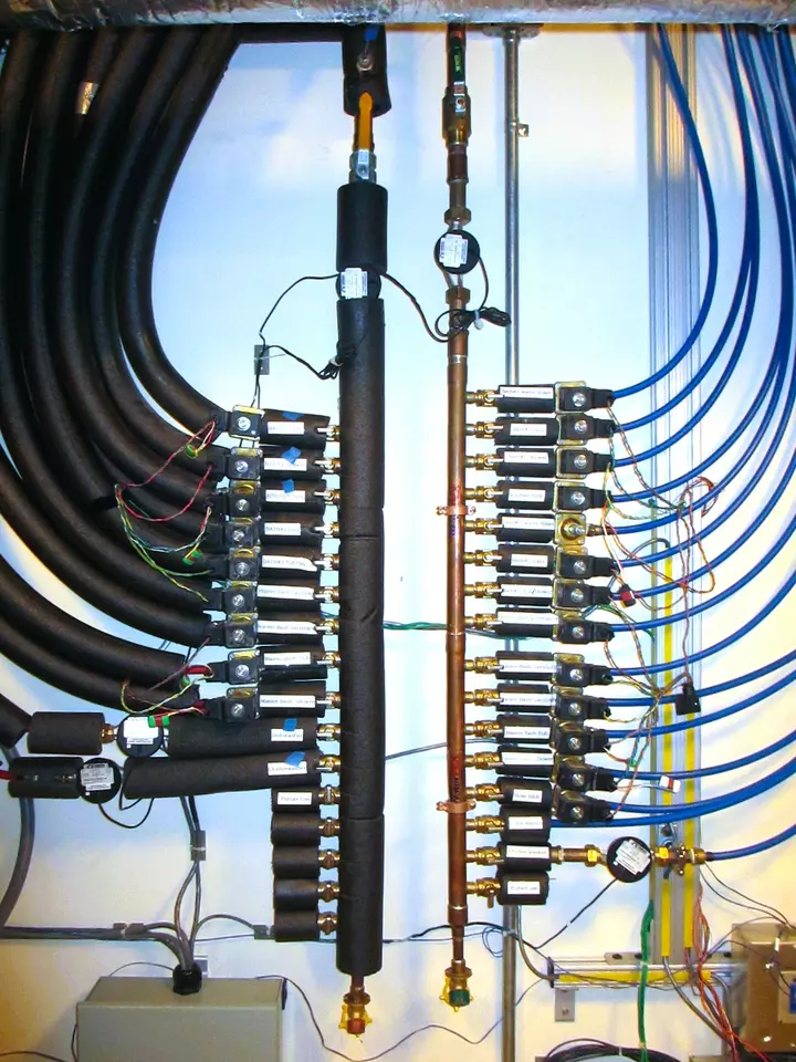 Two parallel vertical pipes are each connected to many others leading off horizontally in opposite directions. The connecting pipes on the left are insulated with black foam.