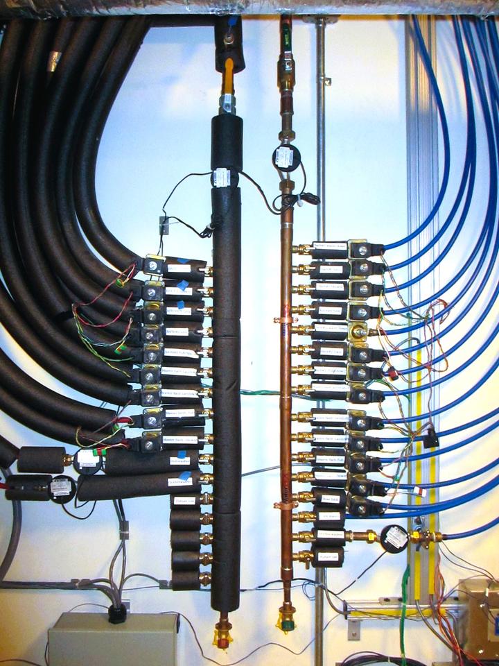 Two parallel vertical pipes are each connected to many others leading off horizontally in opposite directions. The connecting pipes on the left are insulated with black foam.