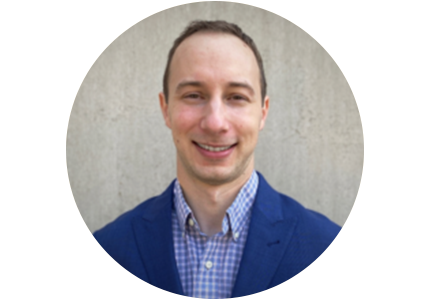 person with very short brown hair wearing a blue suit jacket and a dress shirt 