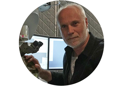 person with short white hair and a short white beard, working with a scientific instrument