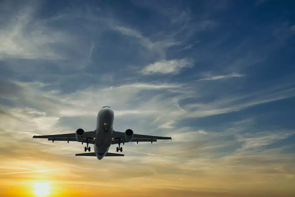 A passenger airplane seen from below takes off in front of a setting sun. 