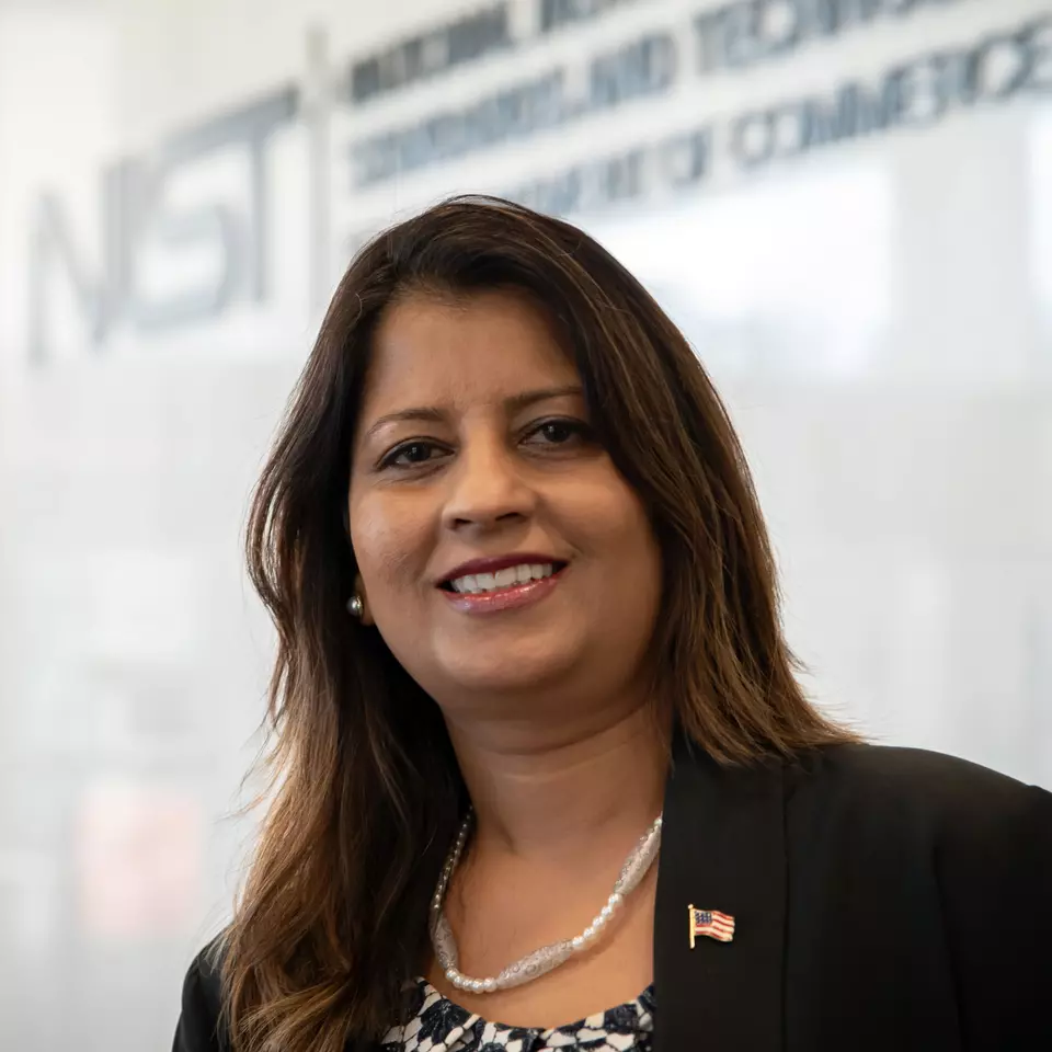 Photo of a woman standing in front of a sign displaying the NIST logo.