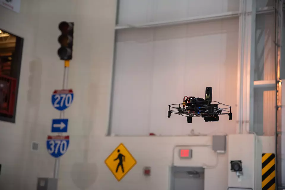 UAS in air inside a testing facility that includes street signs and stoplights. 