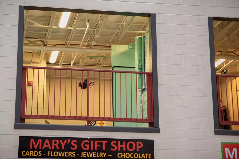 A drone is flying inside a second-story balcony space in a testing facility that includes pretend storefronts like Mary's Gift Shop. 