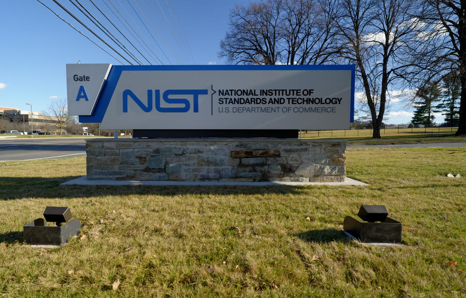 Outdoor sign with trees and telephone wires in background reads: NIST: National Institute of Standards and Technology: Gate A