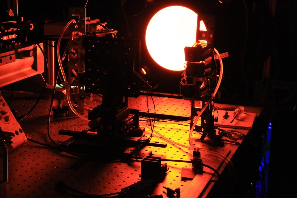 A circular light shines in a darkened lab, with equipment and wiring in the foreground.
