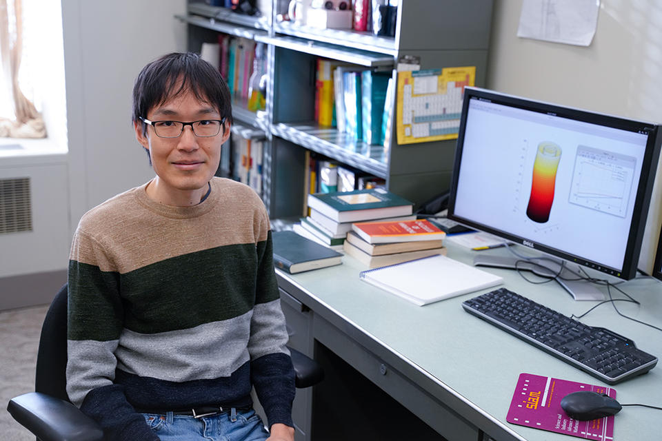 A researcher poses at his desk with a computer screen showing a cylindrical model of an esophagus. 