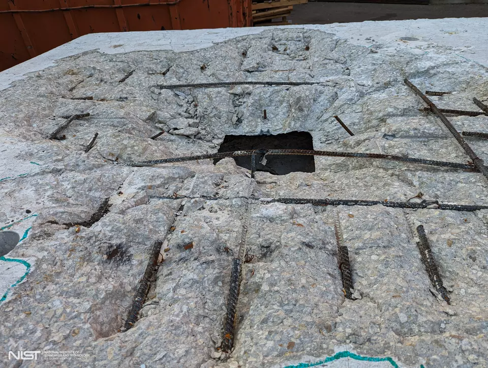 A slab of concrete has had the surface sheared off, exposing a grid of rebar and a center hole. 