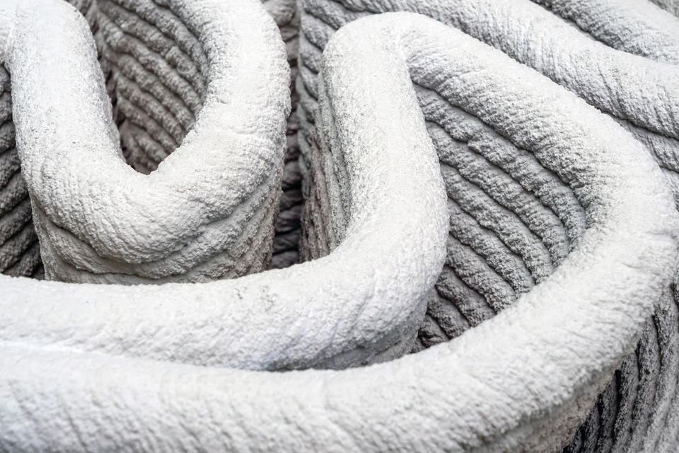 Closeup view of a 3D printed concrete wall. Layers of zigzagging concrete build up to form a structure.