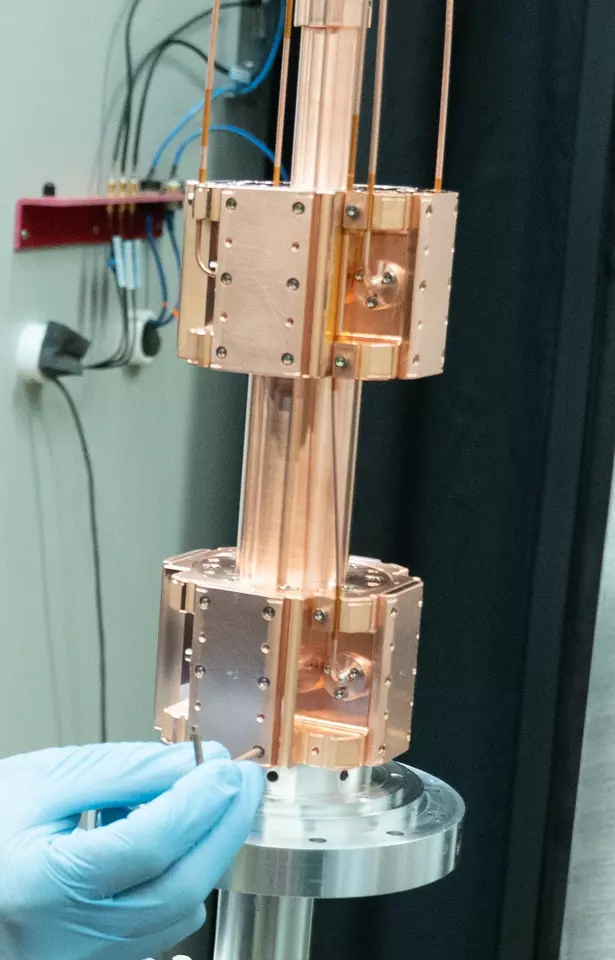 A copper-colored metal device has a vertical tube running through two separate chambers.