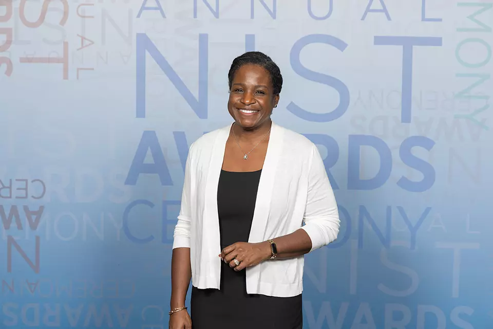 Melissa Taylor poses smiling in front of a banner for the NIST Awards Ceremony.