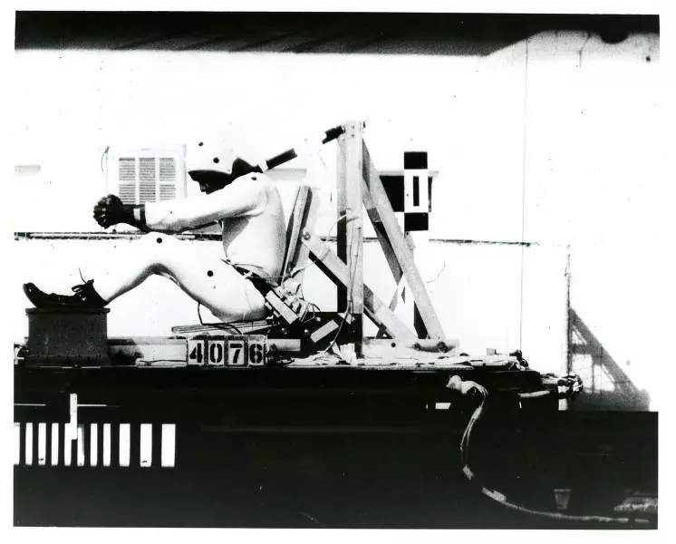 Historical photo shows test subject in helmet and bodysuit strapped into moving seat.