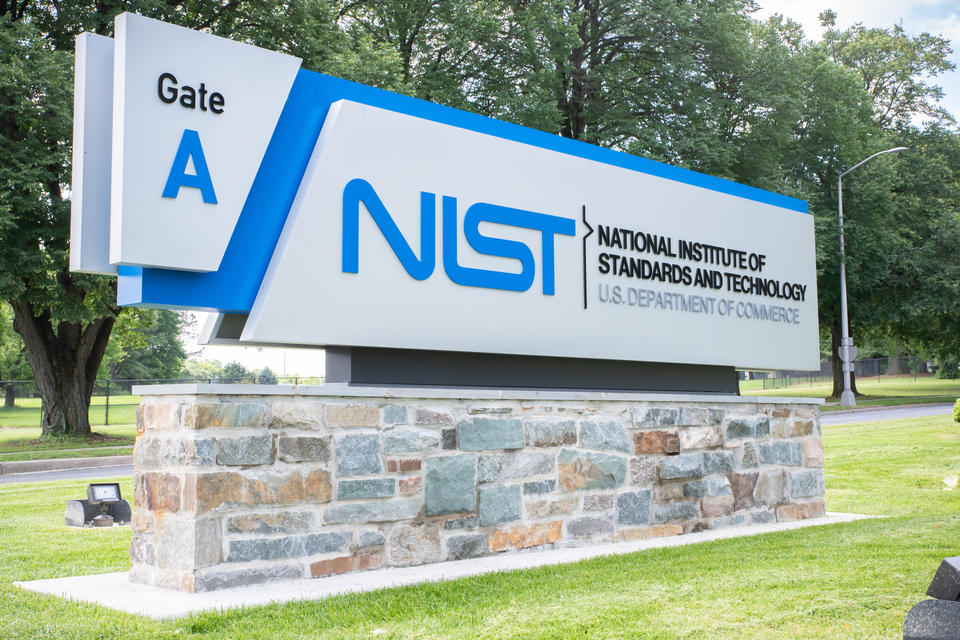Outdoor entry sign with trees in background reads "NIST U.S. Department of Commerce, Gate A."