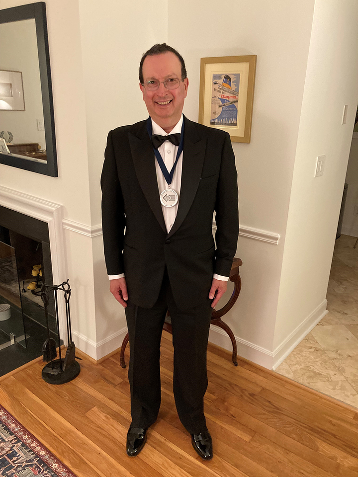 Alex Maranghides, wearing a tuxdeo and displaying his Sammies medal, stands and looks at the camera.
