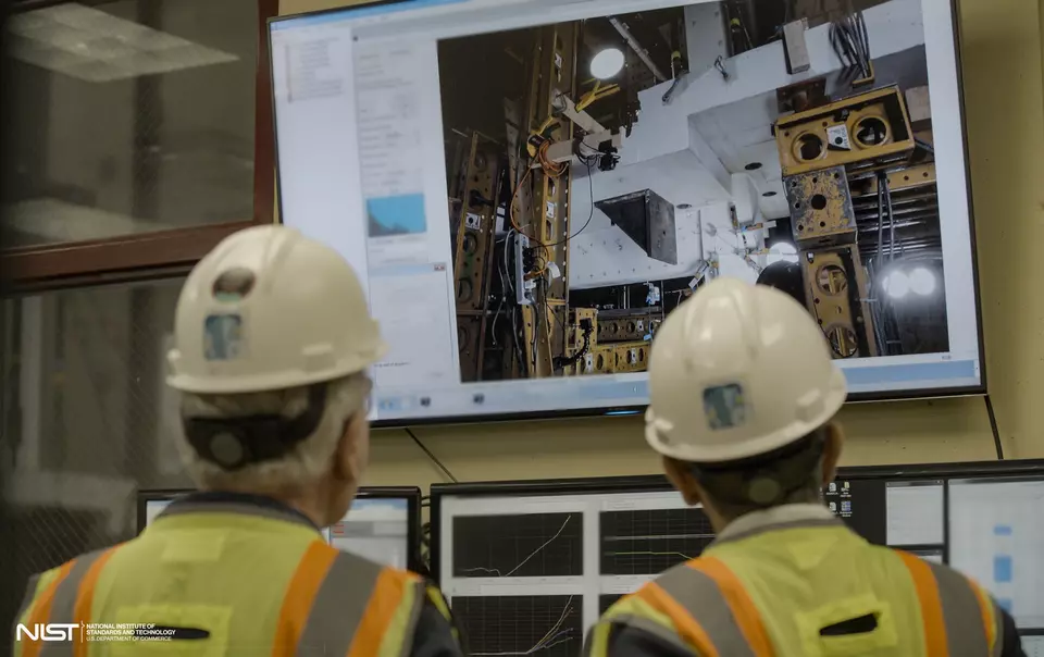 Two people in hard hats, shown from behind, look at a large screen showing concrete slabs and testing equipment.