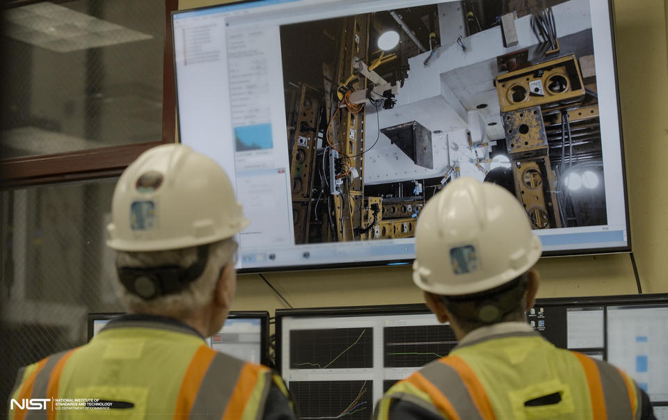 Two people in hard hats, shown from behind, look at a large screen showing concrete slabs and testing equipment.