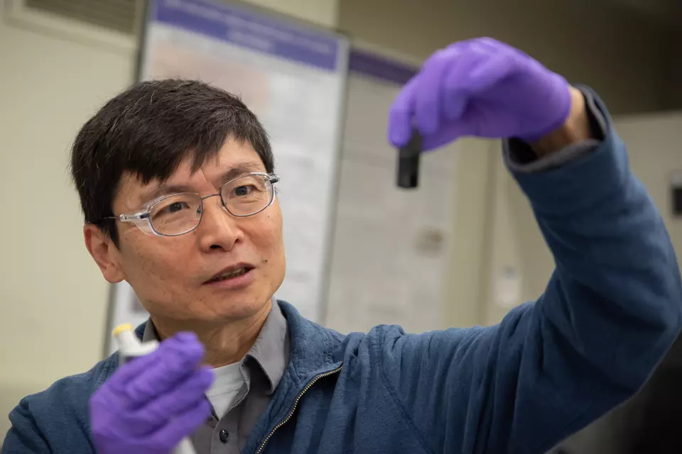 Researcher Ming Zheng looks with interest at a small vial he is holding up in front of him. 