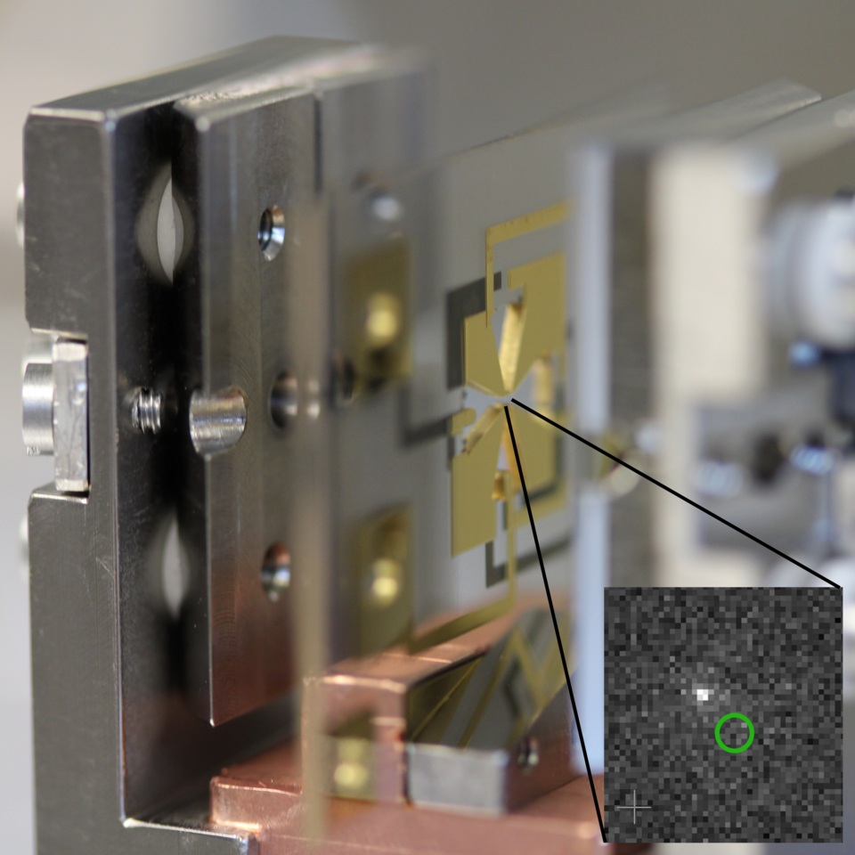 Close-up photo of metal plate holding flat gold-colored device. Inset shows gray pixelation with green circle.  