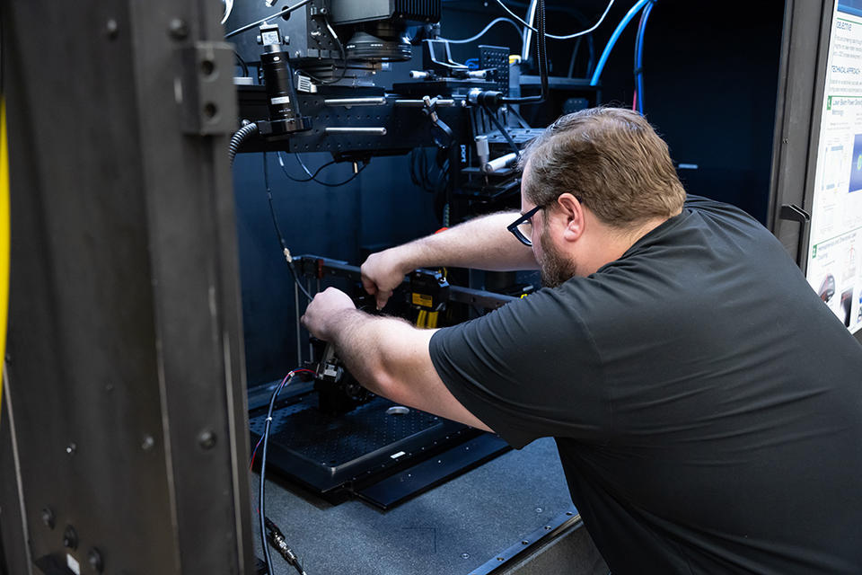 View from over a man's shoulder shows him adjusting scientific equipment inside a cabinet. 
