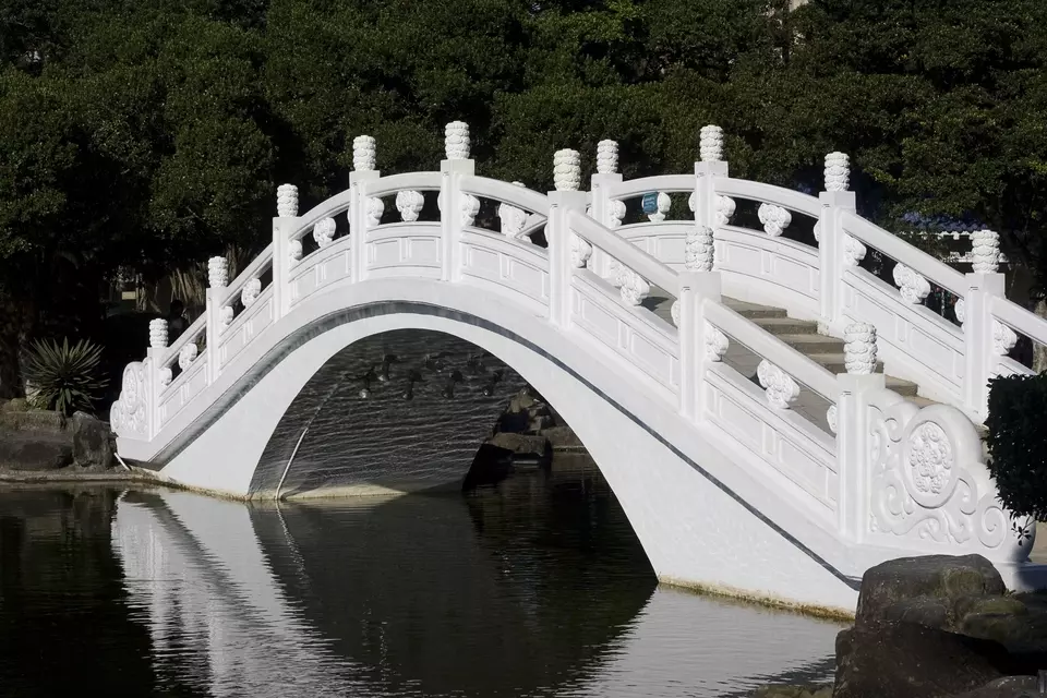 Chinese-style bridge going over a pond. The underside of the bridge shows rippling reflections. 