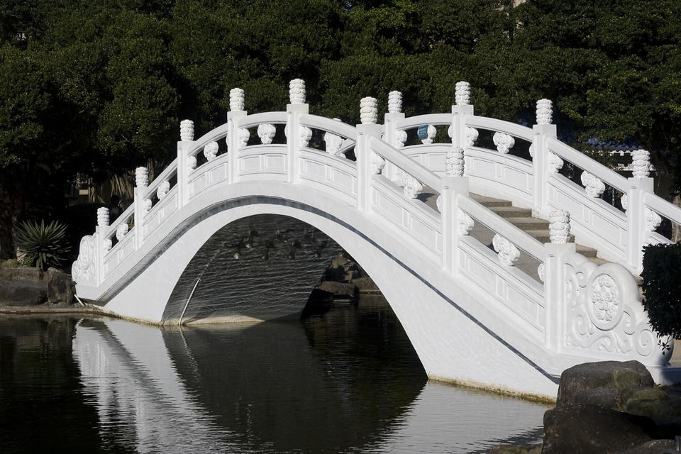 Chinese-style bridge going over a pond. The underside of the bridge shows rippling reflections. 