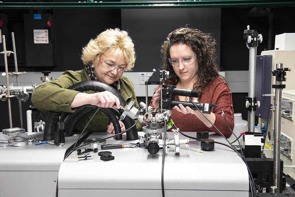 Angie Hight Walker and Amber McCreary stand side by side in the lab adjusting a complex scientific device.