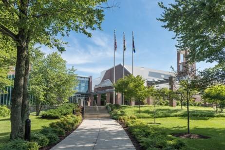 Outdoor photo of a walkway leading up to a building with three flag poles