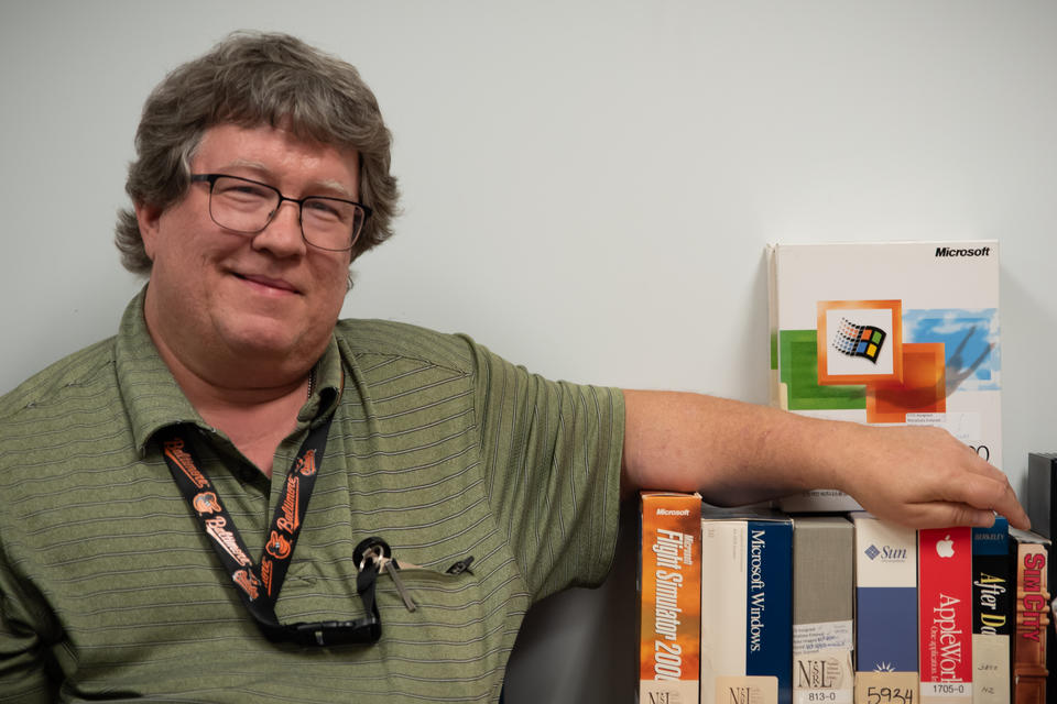 Doug White poses with his arm resting on a row of software boxes. 