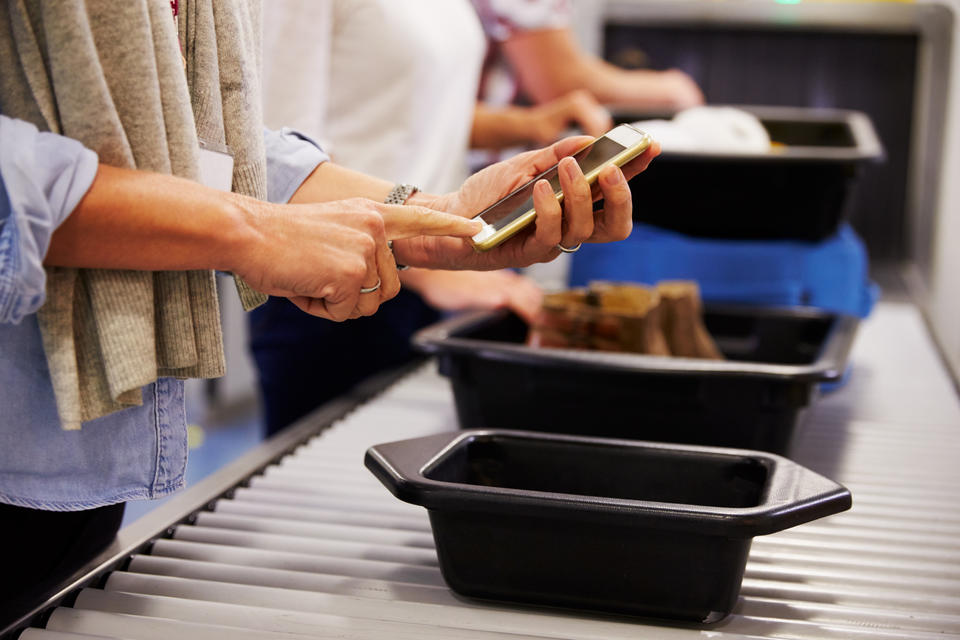 A person in an airport security line turns off their phone in preparation for putting it into a plastic tub to go through the scanner. 