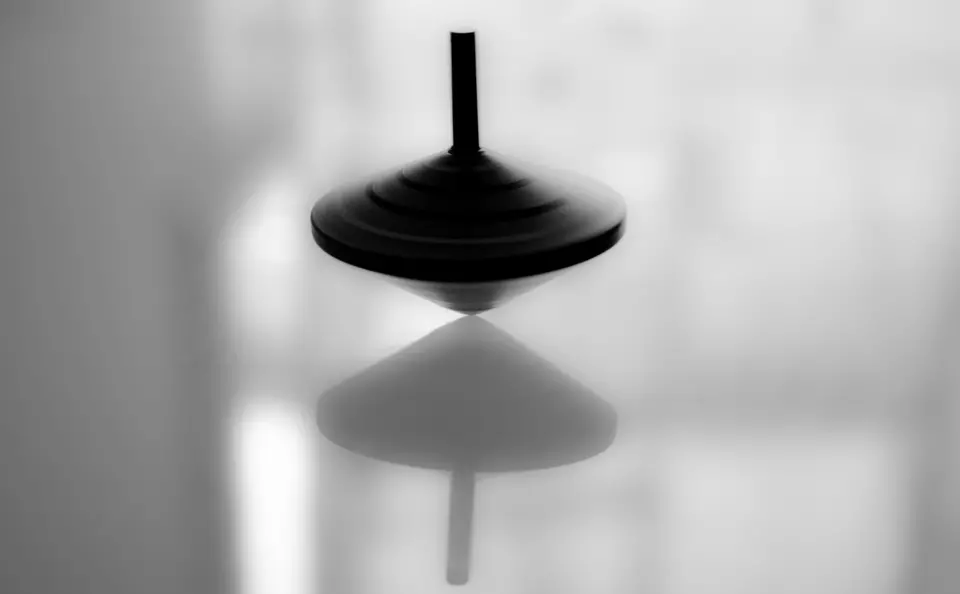Black and white image of a spinning top on a mirrored surface.