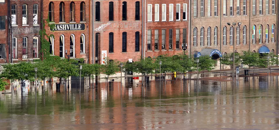 Floodwaters rise to the doorways of a row of historic brick buildings, one with a sign saying "Nashville."