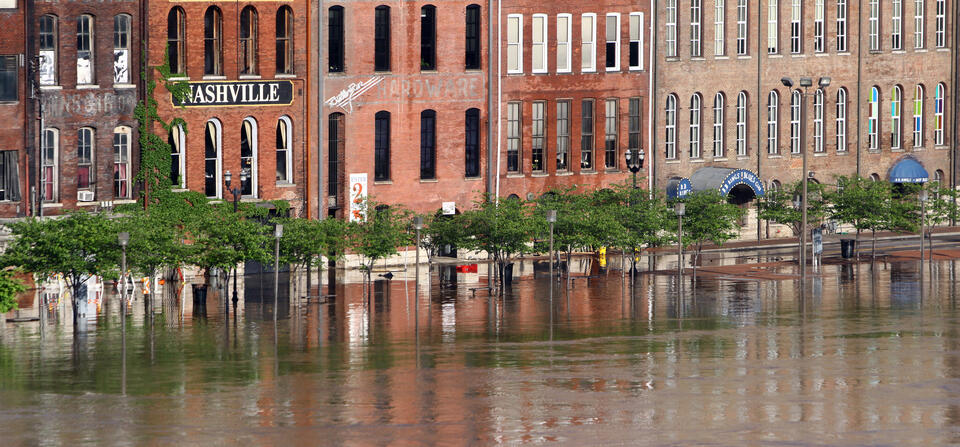 Floodwaters rise to the doorways of a row of historic brick buildings, one with a sign saying "Nashville."
