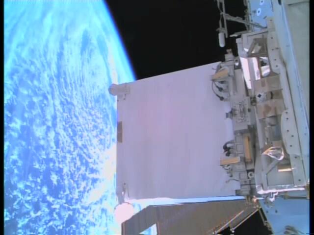 A white box is attached to the ISS in outer space with the curve of the Earth in the background. 