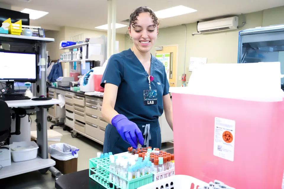 A medical worker in scrubs places a vial into a rack in a medical lab. 