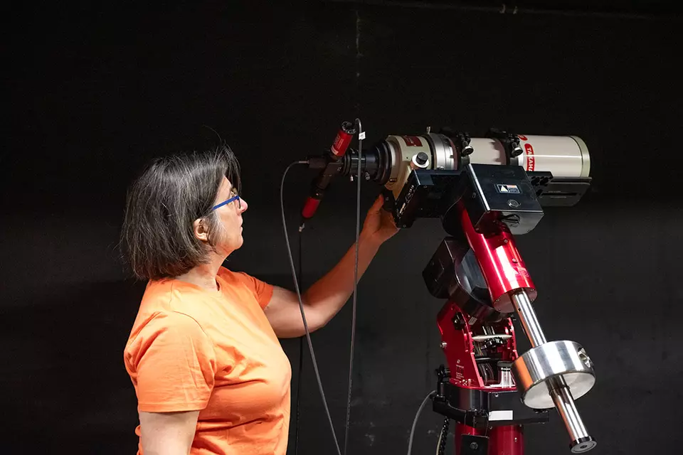 Susana Deustua looks at a large, red telescope located in a dark room. 