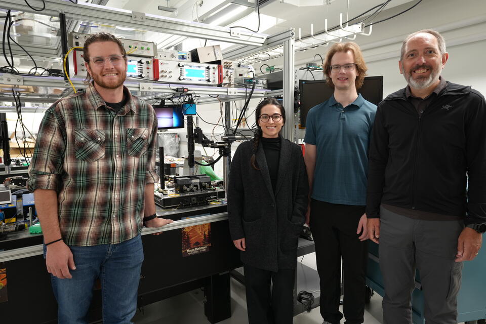 Four researchers pose smiling around a laser device on a lab table. 