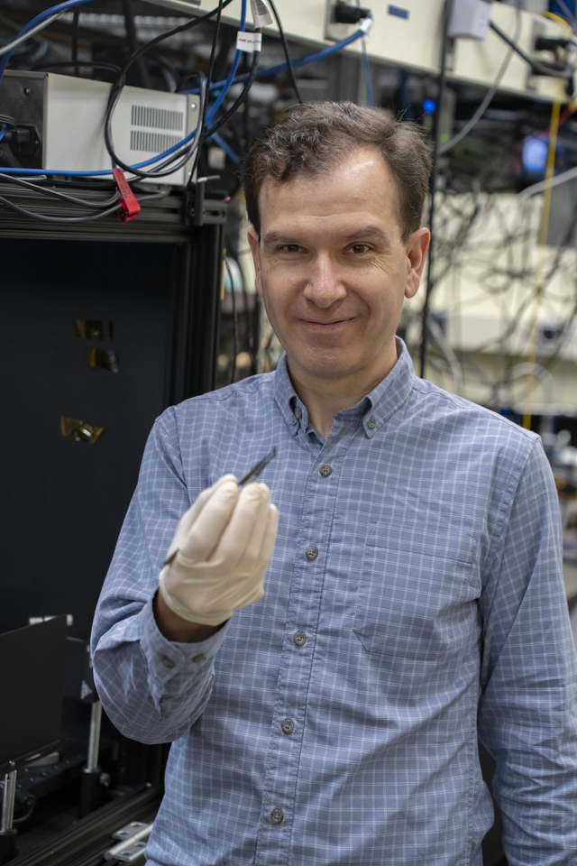 A researcher stands in the lab, holding a chip with tweezers in his gloved hand. 