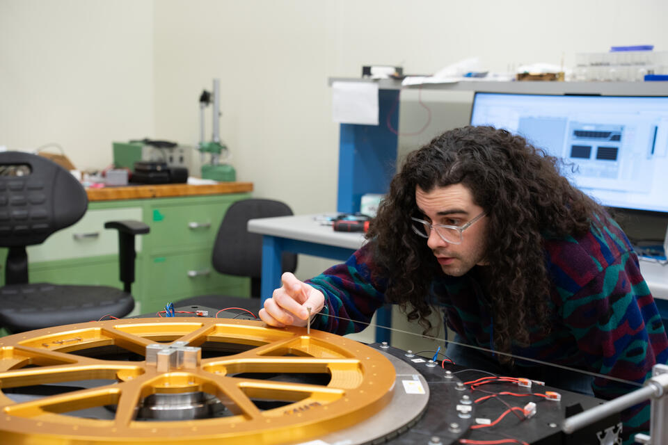 A researcher adjusts a small item on top of a scientific device with a large circular piece lying flat on top. 