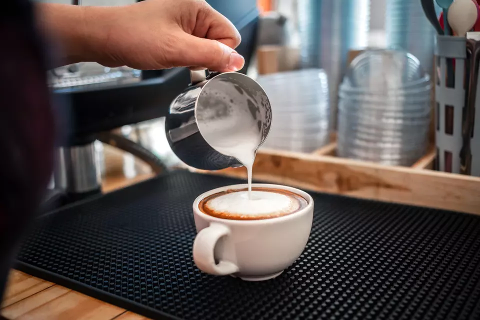 A barista pours steamed milk into a cup of espresso.