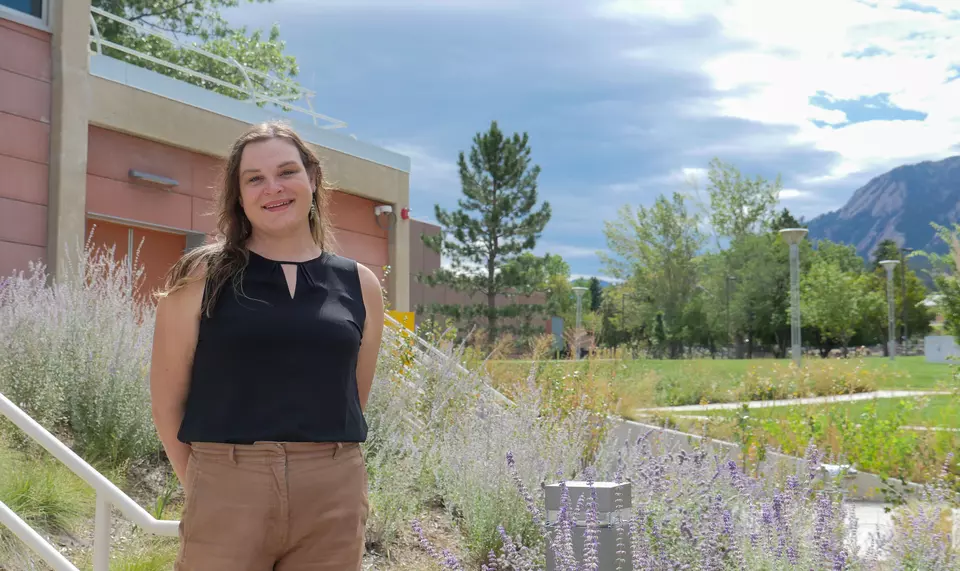 Image of a female researcher standing in front of a building with mountains in the background. 